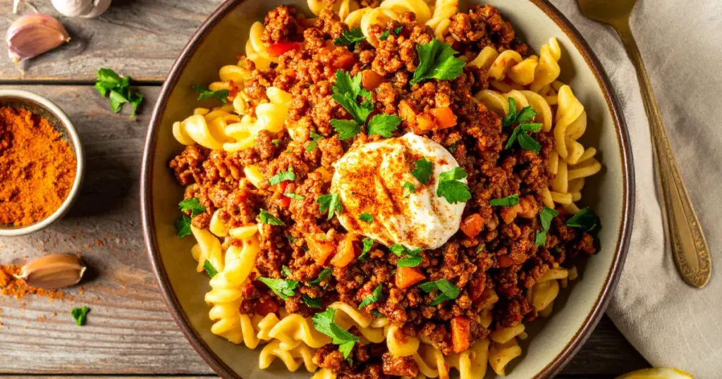 Ground beef recipes Instant Pot style featuring a creamy beef and noodle dish, topped with yogurt sauce and fresh herbs, served in a white bowl on a rustic wooden table.